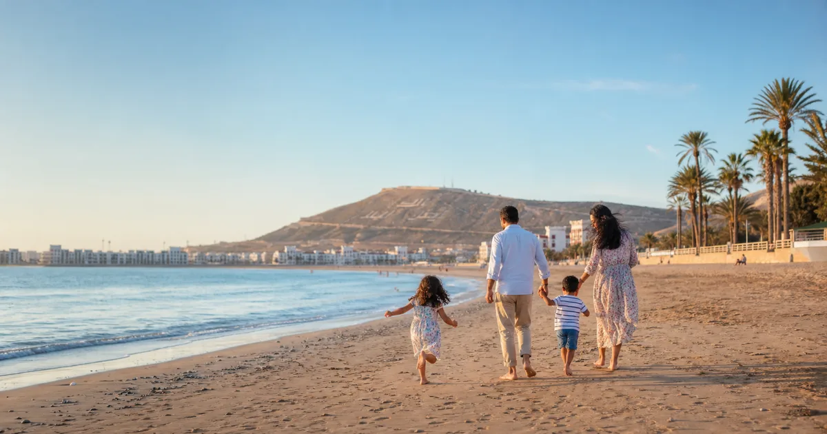 Famille marchant sur la plage d'Agadir au coucher du soleil, baie de sable doré et palmiers en bord de promenade