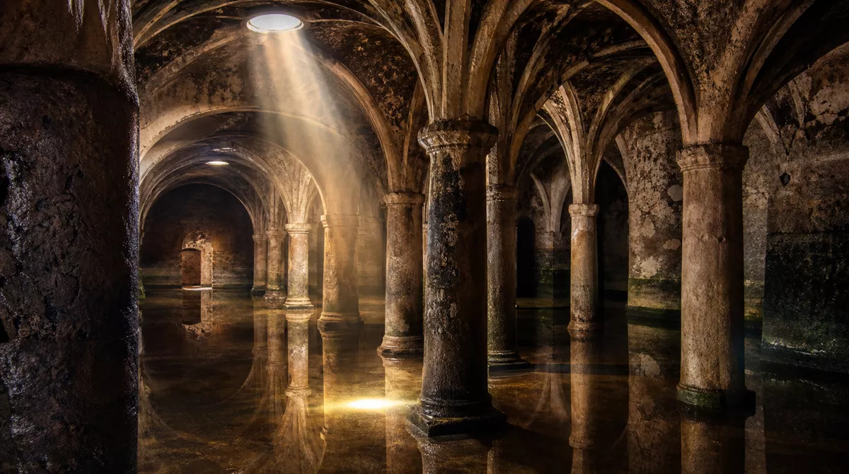 El Jadida cistern interior with Portuguese stone arches reflected in shallow water and a dramatic light beam from the circular roof opening