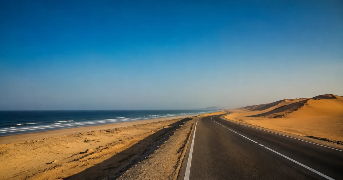 Route désertique longeant l’Atlantique vers le sud après Dakhla, avec des dunes dorées à perte de vue sous un ciel immense