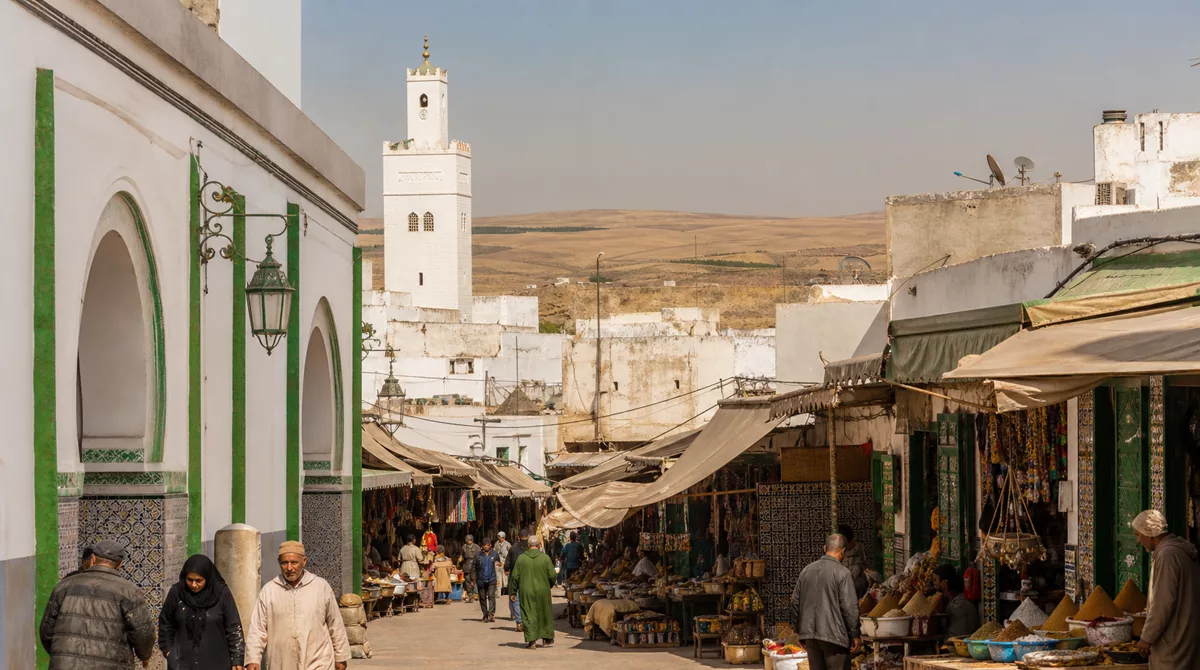 Oujda medina gate at golden hour with traditional Moroccan architecture, palm trees and a lively street scene